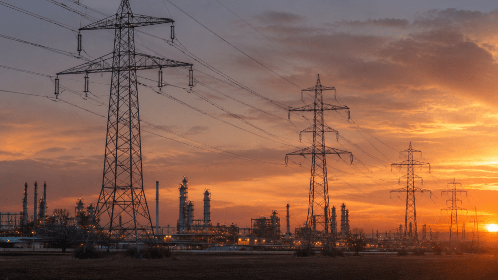 Hochspannungsmasten und Stromleitungen vor einem Industriegebiet in der Abenddämmerung
