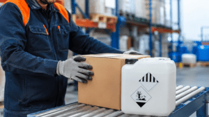 Logistik-Mitarbeiter prüft in einem Versandlager einen Versandkarton und einen Kunststoffkanister als Gefahrgutverpackung.